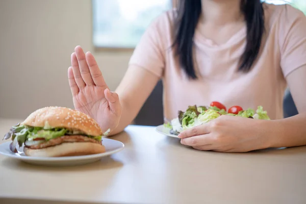 健康的亚洲女人推着一个汉堡包盘 选择吃沙拉 根据饮食计划及清洁食物 避免进食脂肪及含反式脂肪的零食 — 图库照片