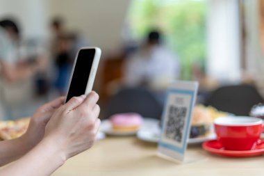 Kadınların elleri yemek menüsünü seçmek için QR kodunu tarıyor. İndirim için tarama yap ya da yiyecek için ödeme yap. Para transferi için telefon kullanma ya da nakit olmadan internet üzerinden para ödeme kavramı..
