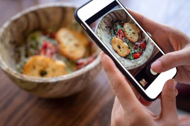 Kadın eli restorandaki yemek masasında yemek fotoğrafı çekmek için bir cep telefonu kullanıyor. Cep telefonu kavramlı fotoğrafçılık