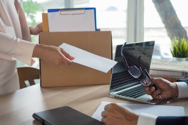 Bir bayan çalışanın elinde bir kutu kişisel eşyası vardır ve bir yöneticiye ya da müdüre istifa mektubu gönderir. İstifa, açık pozisyon ve iş değişiklikleri hakkında bilgi içerir.