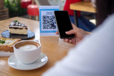 Bir kadın siparişi aldıktan sonra yemek parasını ödemek için QR kodunu tarıyor. Kafe veya lokantada yeni normal ödeme biçimi