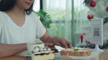 Güzel bir kadın düzen için barkodları tarar. Kafedeki kahve ve pastaneyi taramak için cep telefonlarını kullanan kadınlar. Tarama kodu ile ödeme teknolojisi sosyal mesafeye yardımcı olur..