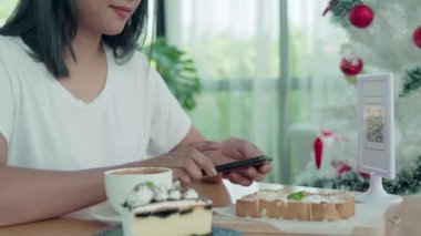 Güzel bir kadın düzen için barkodları tarar. Kafedeki kahve ve pastaneyi taramak için cep telefonlarını kullanan kadınlar. Tarama kodu ile ödeme teknolojisi sosyal mesafeye yardımcı olur..