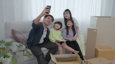 Aile babası, küçük kızı ve oğlu yeni evdeki oturma odasındaki koltuğa oturup gülümseyen ve neşeli bir kahkaha eşliğinde akıllı telefonla selfie çekiyorlar..