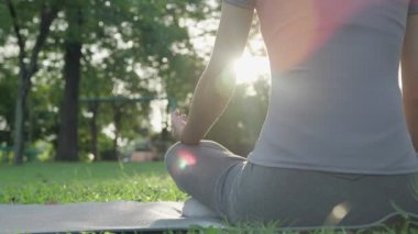 Kadın parkta meditasyon yapıyor. Sabahları egzersiz yapan Asyalı bir kadın. denge, dinlenme, rahatlama, sakinlik, sağlık, mutluluk, rahatlama, sağlıklı yaşam tarzı, stresi azaltma, huzur, tutum.