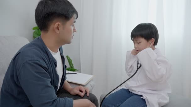 父亲和儿子在每周的假日活动中玩耍 一个男孩在扮演医生的角色 检查他父亲的健康状况 梦想职业概念 — 图库视频影像