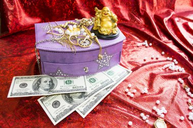 Box for jewelry, dollars and golden Buddha on red background clipart