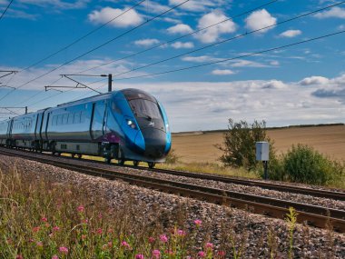 Northumberland, İngiltere 'de hızla giden bir Transpennine Ekspres treni, güneşli bir günde beyaz bulutlarla birlikte alınır..
