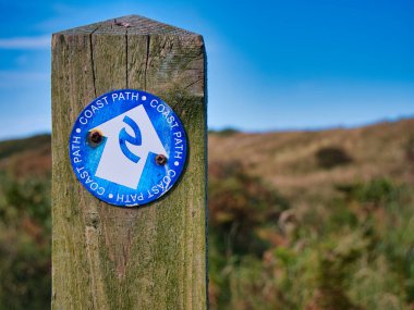 İngiltere 'nin kuzeydoğusunda Northumberland Sahil Yolu' nun üzerindeki eski ahşap bir direğe sabitlenmiş dairesel, mavi ve beyaz bir tabela.