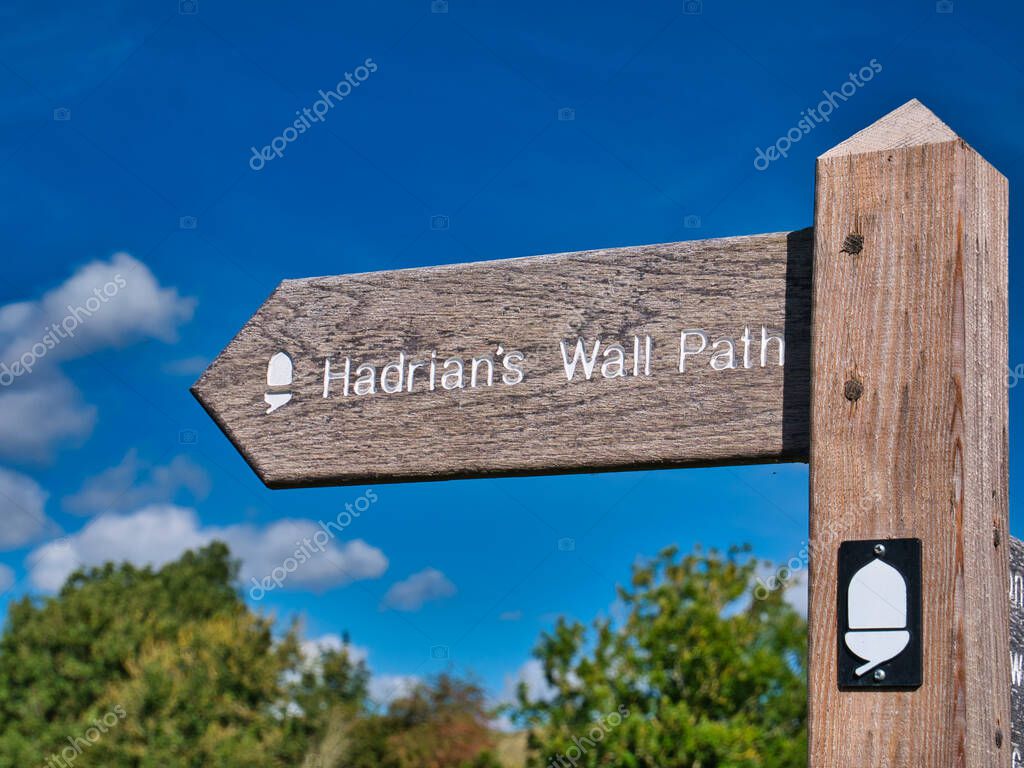 A weathered, wooden signpost points the way of Hadrian's Wall Path, a National Trail in the UK. Taken on a sunny day with a blue sky.