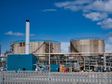 Wirral, Merseyside, İngiltere 'de asfalt üretim tesisinde güvenli bir alanda kimyasal depolama tankları ve bir baca. Yazın güneşli bir günde çekilmiş..