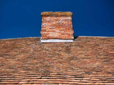 İngiltere, İngiltere 'de güneşli bir günde mavi gökyüzü ile alınan geleneksel bir kır çatısındaki eskimemiş, eski kil kiremitler ve bacalar. Bacanın ve çatının ekleminde kurşun parlaması görülebilir..