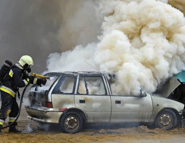 İtfaiyeci, trafik kazasından sonra yanan bir araba kazasının yanında çalışıyor.