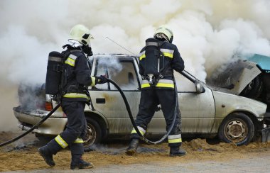 İtfaiyeci, trafik kazasından sonra yanan bir araba kazasının yanında çalışıyor.