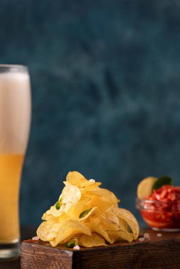 Bir yığın kızarmış patates cipsi, yeşillik, domates sosu ve bir bardak light bira, yakın plan.