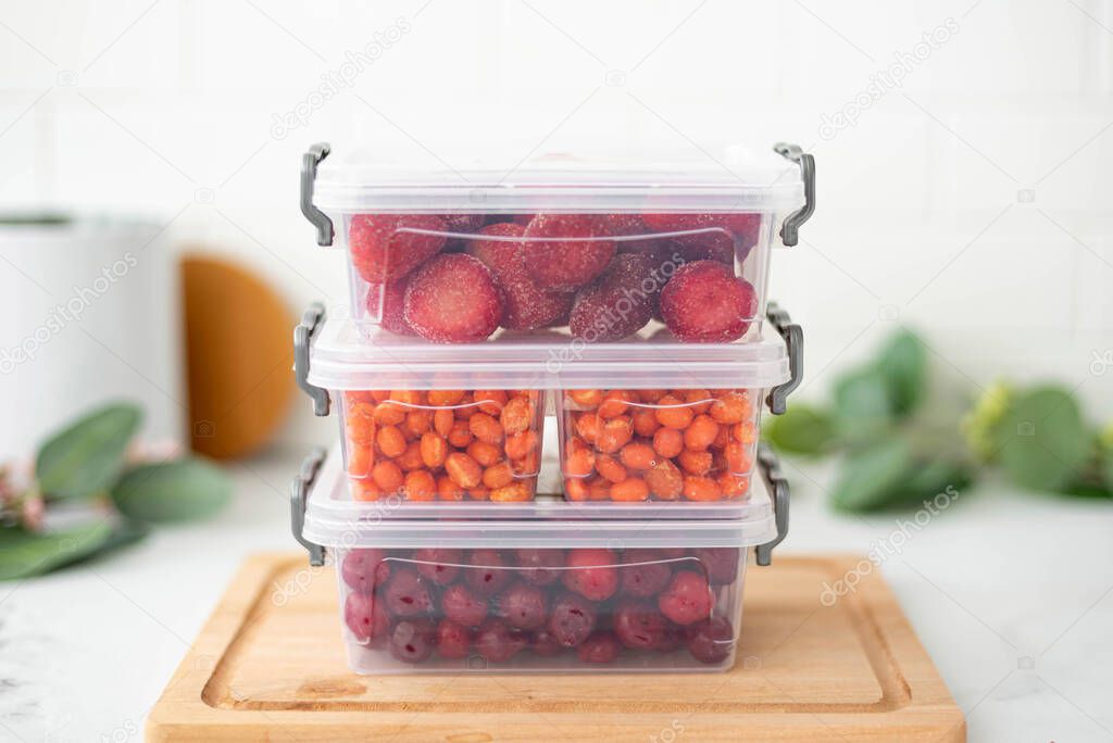 three plastic containers with frozen berries on the kitchen table, close-up