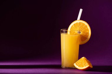 Mor arka planda taze sıkılmış portakal suyu ve portakal dilimleri, yakın plan.