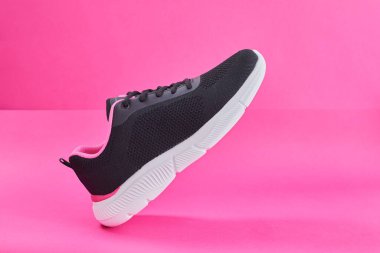 Pembe arka planda koşmak için kadın ayakkabıları. Moda siyah koşu ayakkabısı, spor ayakkabı ya da antrenör. Kadın fitness, spor, eğitim konsepti.