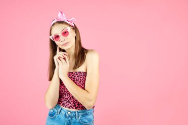 Havalı hippi kız şık gözlük takıyor. Pembe arka planda kameraya bakan olumlu genç bir kadın. Beyaz kadın üniversite öğrencisi pozu. Güzellik aksesuarlarıyla günlük tarz.