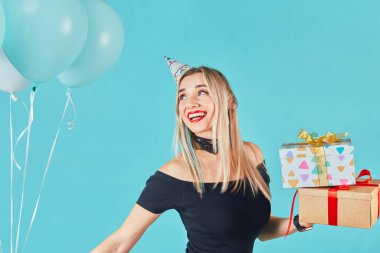 Mavi arka planda doğum günü şapkalı komik kız. Pastel arka planda izole edilmiş testisleri olan parti konisi giyen çekici, neşeli bir kızın yakın plan portresi..