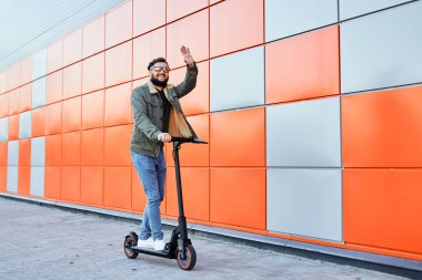 Güneş gözlüklü sakallı adam arka planda elektrikli scooter 'da poz veriyor. Tekmeleyen adam scooter sürüyor..