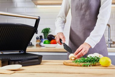 Gri önlüklü bir kadın elektrikli ızgarada mantar pişiriyor. Yemek pişirme süreci kavramı. Sağlıklı yemek.