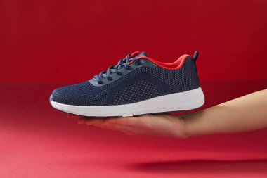 Kırmızı arka planda el ele tutuşan spor ayakkabıları. Koşmak için yeni moda spor ayakkabıları tutuyorum. Yeni spor ayakkabıları seçip almak.