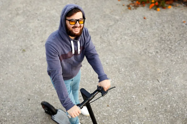 電動スクーターに乗る髭のスタイリッシュな男 毎日の通勤マイクロスクーターに乗って男 スタイリッシュな服装の男性は通りの電子スクーターに立つ — ストック写真