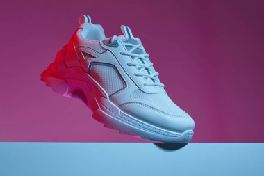 Modern beyaz ayakkabılar, çok renkli, parlak mor neon arka planda izole edilmiş. Deri ayakkabılar çivili büyük tabanda..