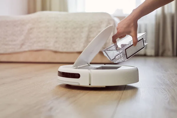 Elektrikli süpürgenin pislikten temizlenmesi için filtre hazırlanıyor. Kadın eli robotik temizleyiciyi açar ve oturma odasında konteynırı tutar..