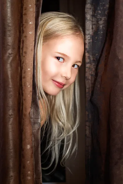 Little girl plays at hide-and-seek looks out because of curtains — Stock Photo, Image