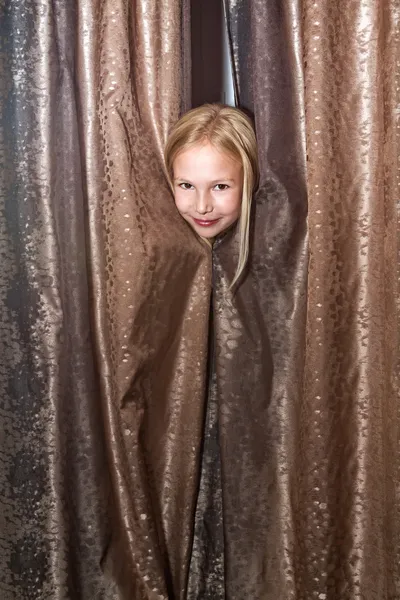 Klein meisje speelt bij verstoppertje kijkt uit vanwege gordijnen — Stockfoto