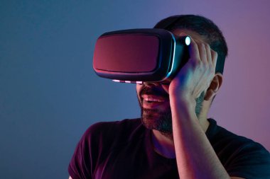 VR gözlüklü genç adam sanal gerçeklikle etkileşim içinde. Renkli neon ışığı, geleceğin teknolojisi, eğitim video oyunu.