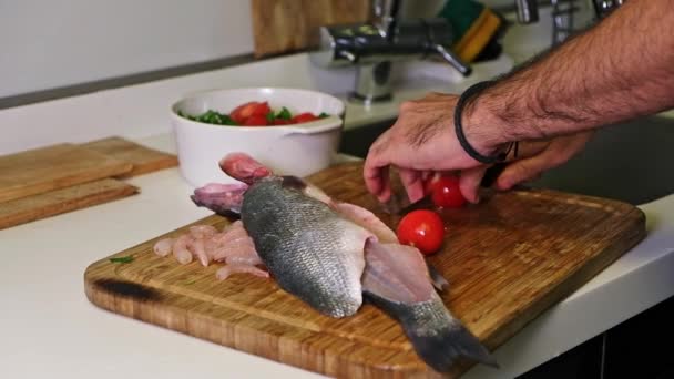 Roher Dorado-Seebarschfisch, bereit zum Kochen auf Schneidebrett. Tomaten für Salat mit Messer schneiden — Stockvideo