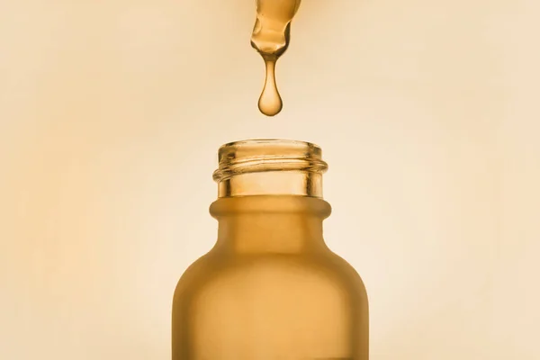 Face serum oil drop with dropper glass bottle pipette on yellow background close up — Stock Fotó