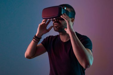 VR gözlüklü genç adam sanal gerçeklikle etkileşim içinde. Renkli neon ışığı, geleceğin teknolojisi, eğitim video oyunu.