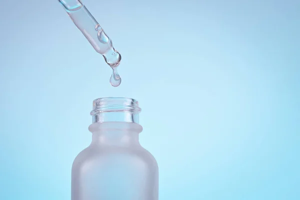Обличчя сироваткове масло краплі з крапельницею скляної пляшки піпетки на синьому фоні крупним планом — стокове фото
