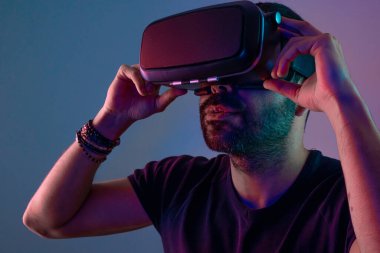 VR gözlüklü genç adam, görsel gerçekliği, renkli neon ışığı, gelecek teknolojisi, eğitim video oyunu ile kapat.