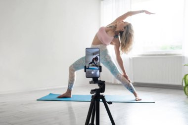 woman practicing yoga poses stretching in front of phone camera sport blogger teacher yoga online