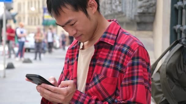Asian man holding smartphone in his hands scrolling screen with news or social media outdoor — 图库视频影像