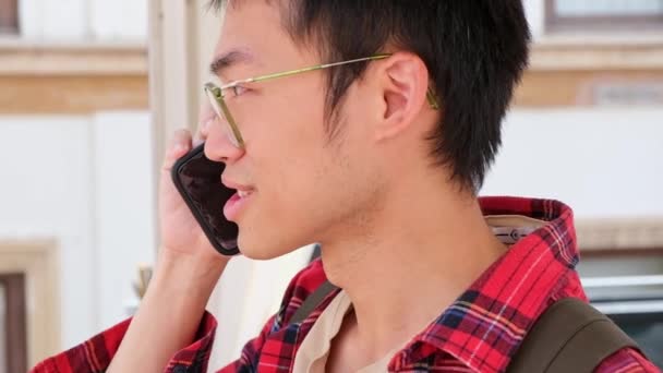 Asian man holding smartphone and talking by phone with friend smiling and laughing outdoor — 图库视频影像