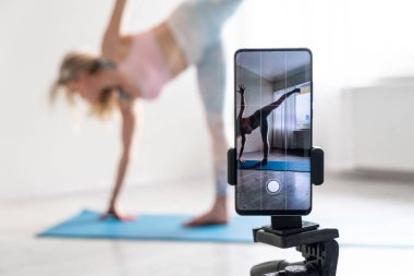 woman practicing yoga poses stretching in front of phone camera sport blogger teacher yoga online