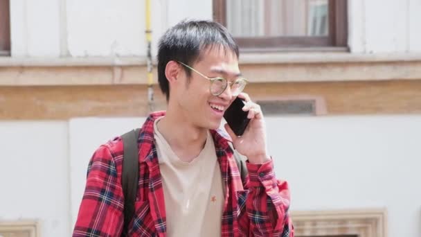 Asian man holding smartphone and talking by phone with friend smiling and laughing outdoor — 图库视频影像