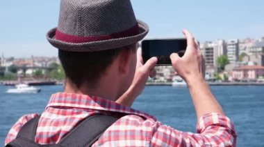 Kırmızı tişörtlü ve şapkalı turist elinde akıllı telefon ve sokak öğrencisi seyahat blogunda İstanbul 'un turistik yerlerinin videosunu tutuyor.