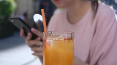 Lezzetli bir bardak taze limonata ve yaz günü kafede cep telefonu kullanan genç bir kadın. Yüksek kaliteli FullHD görüntüler