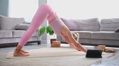 Yoga yapan kadın, evde blog öğretmeni yoga internetteki sağlık koçunda tablet dizüstü bilgisayarın önünde gerinerek poz veriyor.