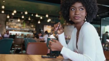 Kafede oturan, kahve içen, gülümseyen, güzel Afro-Amerikan kadın.