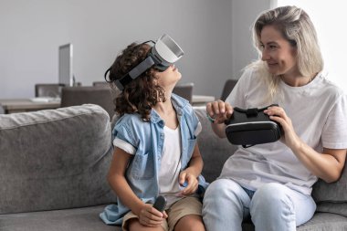 Anne ve oğlu sanal gerçeklik kulaklığı takıyor evdeki oturma odasında sanal gerçeklik oyunları oynayarak eğleniyorlar.