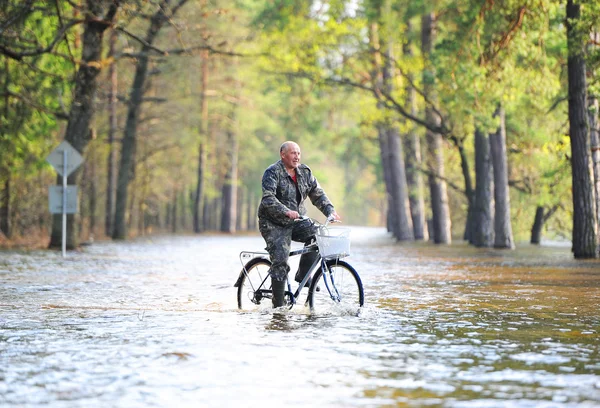 O homem de bicicleta vai na estrada inundada — Fotografia de Stock