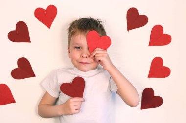 Sevgililer Günü için kırmızı kalbi tutan tatlı küçük çocuk. Beyaz arka planda kırmızı kalpli, gülümseyen çocuk..